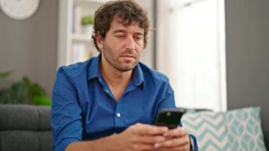 Genç İspanyol adam evde rahim ağrısı için akıllı telefon kullanıyor.