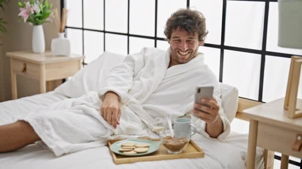 Young Hispanic Man Having Breakfast Watching Video Smartphone Bedroom — Stock Video