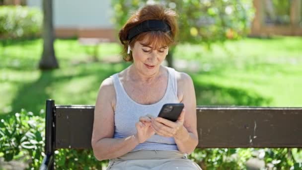 Mujer Mediana Edad Usando Teléfonos Inteligentes Auriculares Sonriendo Parque — Vídeo de stock