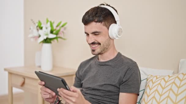 Hombre Hispano Joven Usando Touchpad Auriculares Sentados Cama Dormitorio — Vídeos de Stock