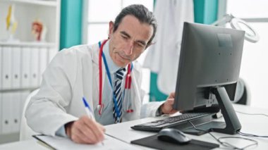Klinikte bilgisayar kullanan orta yaşlı bir doktor.