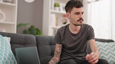 Young hispanic man talking on smartphone using laptop at home
