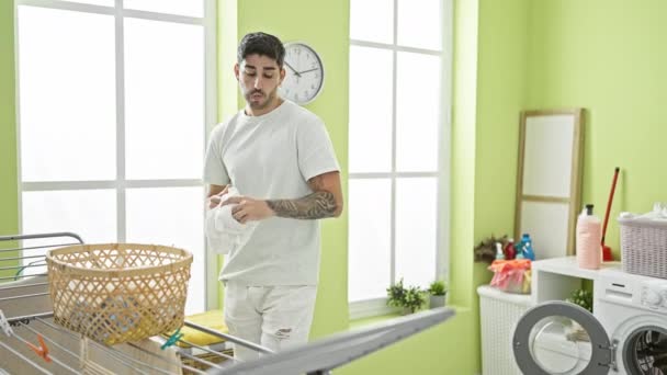 洗濯室で祝う洗濯機に服を投げる若いヒスパニックの男 — ストック動画