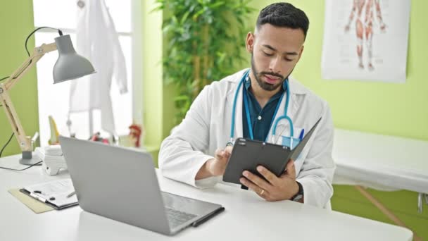 Young Hispanic Man Doctor Using Laptop Working Clinic — Vídeo de stock