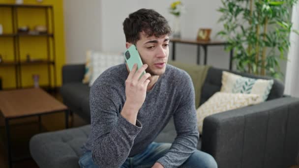 Młody Hiszpan Rozmawiający Przez Telefon Uśmiechający Się Siedząc Kanapie Domu — Wideo stockowe