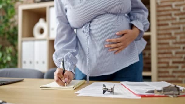 若い妊娠中の女性のビジネスワーカーがオフィスで腹に触れるノートに書く — ストック動画