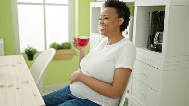 若いです妊娠中の女性はダイニングルームでテーブルの上に座ってコーヒーを飲む — ストック動画