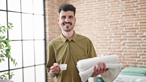 Młody Hiszpan Uśmiecha Się Pewnie Trzymając Złożone Ręczniki Kubek Detergentu — Wideo stockowe