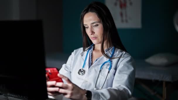 若い美しいヒスパニック系の女性医師がクリニックで働くスマートフォンを使って — ストック動画