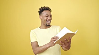 Afro-Amerikalı bir adam gülerek sarı arka planda kendine güvenen bir kitap okuyor.