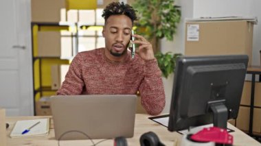 Afrika kökenli Amerikalı bir iş adamı bilgisayarını kullanarak ofisteki akıllı telefondan konuşuyor.