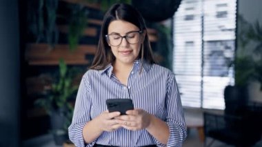 Ofiste akıllı telefon kullanarak mutlu gülümseyen güzel İspanyol kadın.