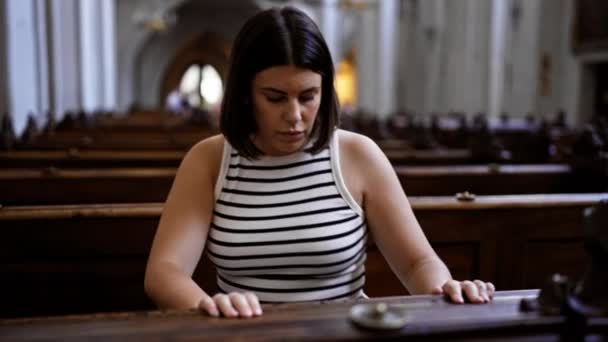 在维也纳奥古斯丁教堂的教堂长椅上祈祷的年轻美丽而惊慌的女人 — 图库视频影像