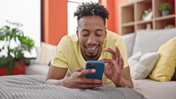 Afrykański Amerykanin Pomocą Smartfona Leżącego Kanapie Domu — Wideo stockowe