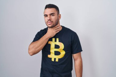 Bitcoin tişört giyen genç İspanyol adam ağrılı boyuna dokunuyor, boğazı ağrıyor grip, mantar ve enfeksiyon kapmış. 