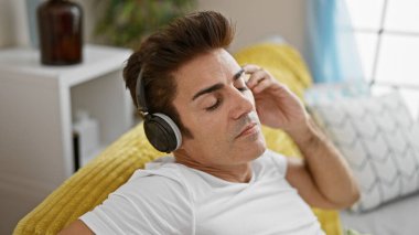Genç İspanyol adam evdeki kanepede oturmuş müzik dinliyor.