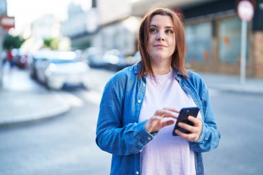 Young beautiful plus size woman smiling confident using smartphone at street