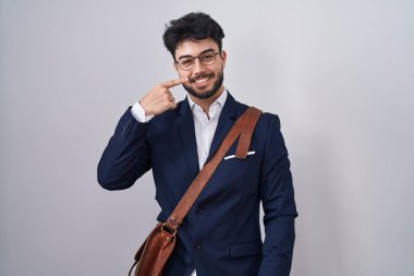 Sakallı, iş elbiseleri giyen, el ve burnu işaret eden, neşeli gülümseyen İspanyol bir adam. güzellik konsepti 