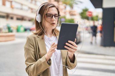 Sokakta dokunmatik ped ve kulaklık kullanan genç bir iş kadını.