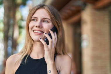 Genç sarışın kadın gülümsüyor. Kendine güveni tam. Akıllı telefondan konuşuyor.