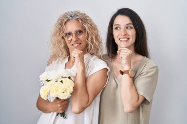Anne ve kızı ellerinde bir buket beyaz çiçekle çeneleri üzerinde soru sorarken düşünceli bir ifade takınıyorlar. Gülümseyen ve düşünceli bir yüz. şüphe kavramı. 