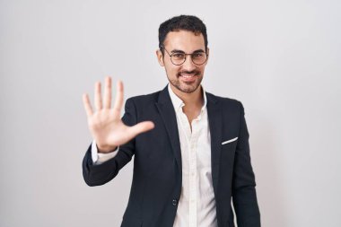 Beyaz arka planda duran yakışıklı İspanyol adam beş numarayı gösterip işaret ederken kendinden emin ve mutlu gülümsüyor.. 