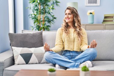 Yoga egzersizi yapan genç bir kadın evdeki kanepede oturuyor.