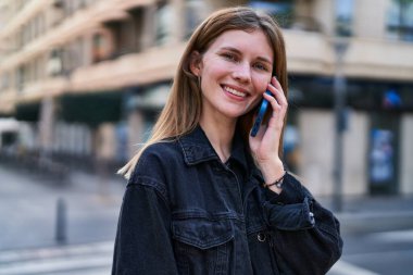 Genç sarışın kadın gülümsüyor. Kendine güveni tam. Akıllı telefondan konuşuyor.