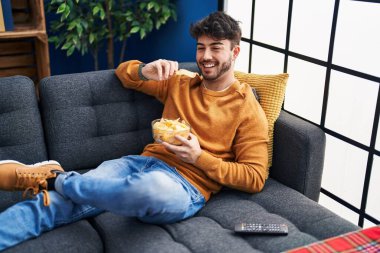 Young hispanic man watching movie sitting on sofa at home