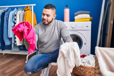 Young latin man smiling confident washing clothes at laundry room