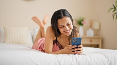 Yatakta uzanmış akıllı telefon kullanan genç, güzel İspanyol kadın.