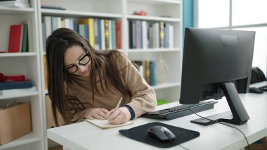 Güzel İspanyol kız öğrenci kütüphanede defter üzerine bilgisayar kullanıyor.