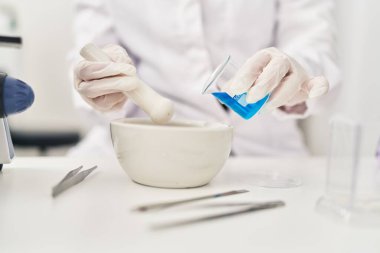 Young beautiful hispanic woman scientist pouring liquid on bowl at laboratory