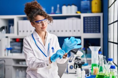 Young hispanic woman scientist smiling confident wearing gloves at laboratory