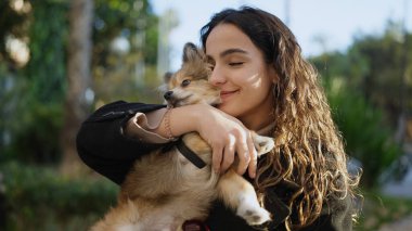 Parkta kendinden emin bir şekilde gülümseyen köpeği olan genç İspanyol kadın.