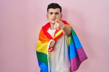 İkili olmayan kişi elinde gökkuşağı lgbtq bayrağı ile kamerayı ve seni işaret ediyor, kendine güvenen hareketin ciddi görünüyor. 