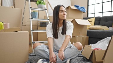 Young beautiful hispanic woman smiling confident sitting on floor at new home