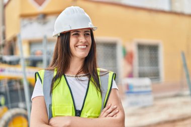 Güzel İspanyol kadın mimar gülümsüyor. Kollarını kavuşturup caddede duruyor.