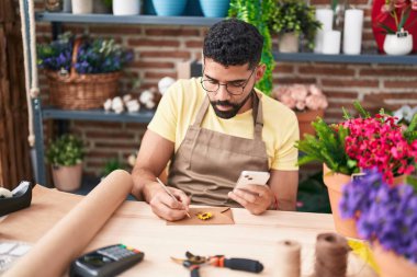 Çiçekçide akıllı telefon kullanarak mektup yazan genç Arap bir çiçekçi.