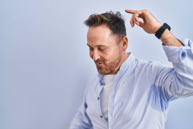 Orta yaşlı beyaz bir adam mavi arka planda dans ediyor mutlu ve neşeli, hareketli ve kendinden emin bir şekilde müzik dinliyor. 