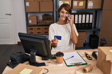 Genç ve güzel İspanyol bir kadın. İş kadını. Ofiste elinde kredi kartıyla akıllı telefondan konuşuyor.