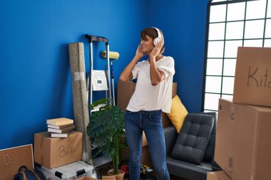 Genç, güzel, İspanyol bir kadın yeni evinde müzik dinlerken kendinden emin gülümsüyor.