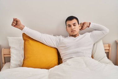 Young man waking up stretching arms at bedroom