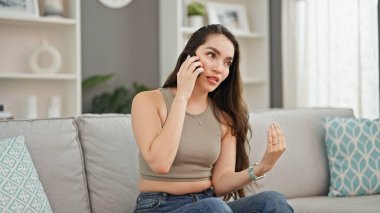 Young beautiful hispanic woman talking on the smartphone with serious expression at home