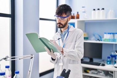Young hispanic man scientist writing on notebook working at laboratory
