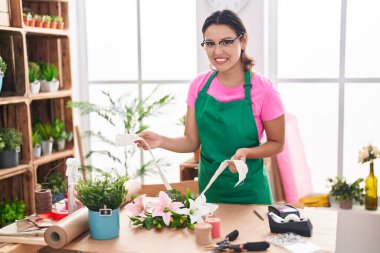 Young hispanic woman florist make bouquet of flowers at florist