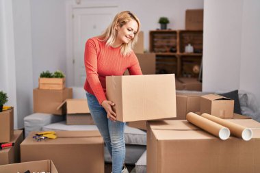 Genç sarışın kadın yeni evinde kendine güvenen bir paket tutuyor.