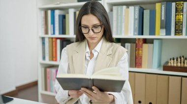 Üniversite sınıfındaki masada oturmuş kitap okuyan güzel İspanyol kadın.
