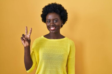 Sarı stüdyonun başında duran Afrikalı genç kadın iki numarayı gösterip işaret ederken kendinden emin ve mutlu bir şekilde gülümsüyor.. 