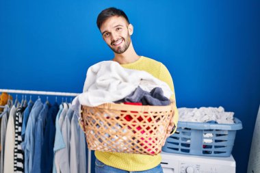Çamaşır odasında çamaşır sepetini tutan kendine güvenen İspanyol genç adam.